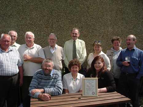 The landlord and landlady of the Fleece receive their award. Seated centre is Jenny Greenhalgh, chairman of Lunesdale CAMRA. Behind her with a tie on is John Jacks, tenant of the Fleece. Seated right is Kim Larsen, the landlady. Other people are CAMRA members and pub regulars.